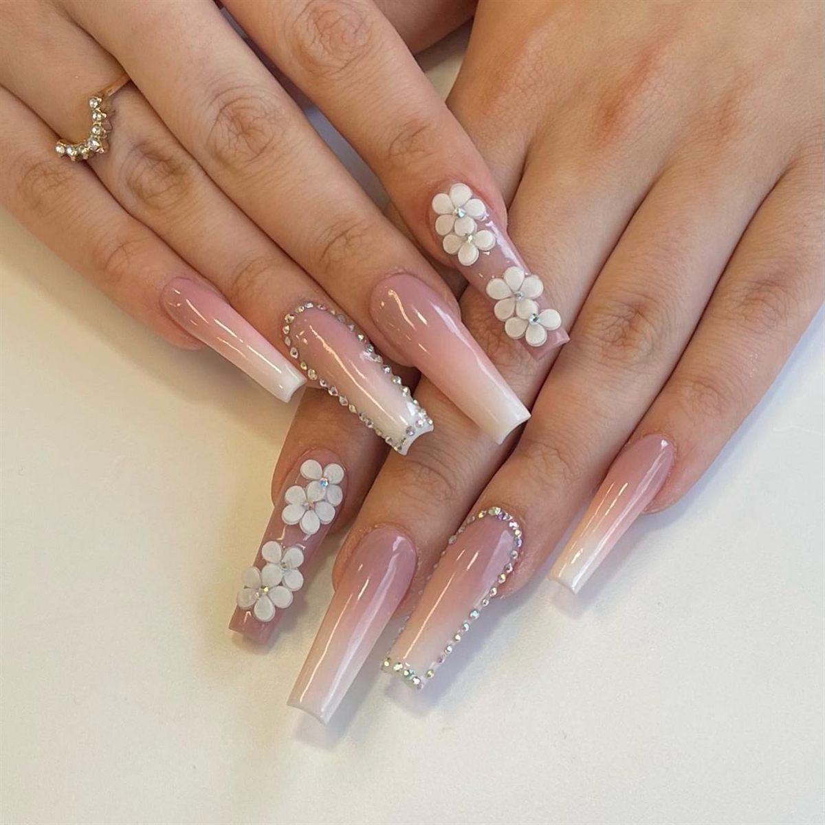 Nude-to-white ombre coffin nails with 3D white flowers and crystal lines
